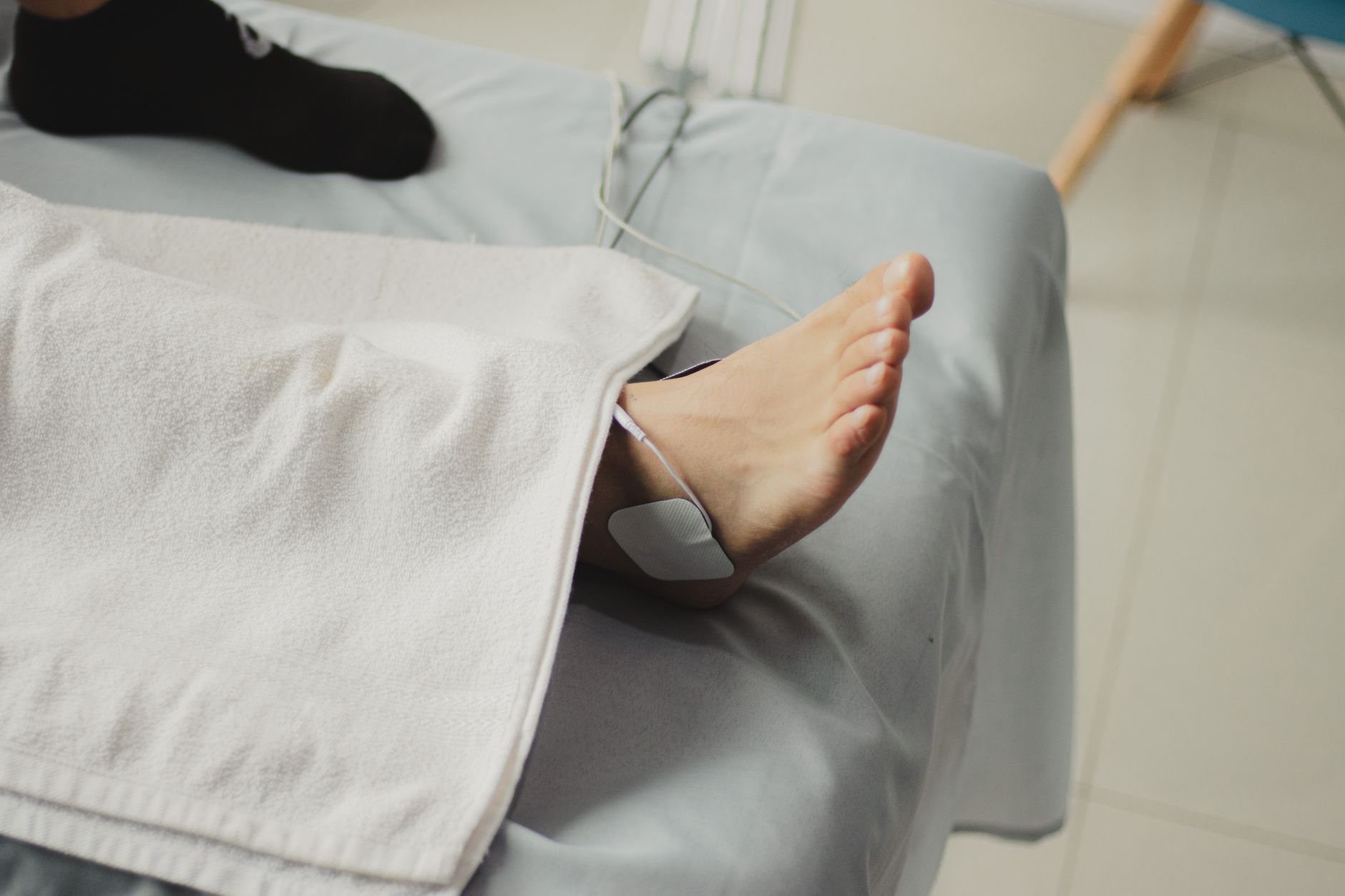 Pacjent leżący w łóżku szpitalnym z elektrodami na stopie podłączonymi do urządzenia terapeutycznego