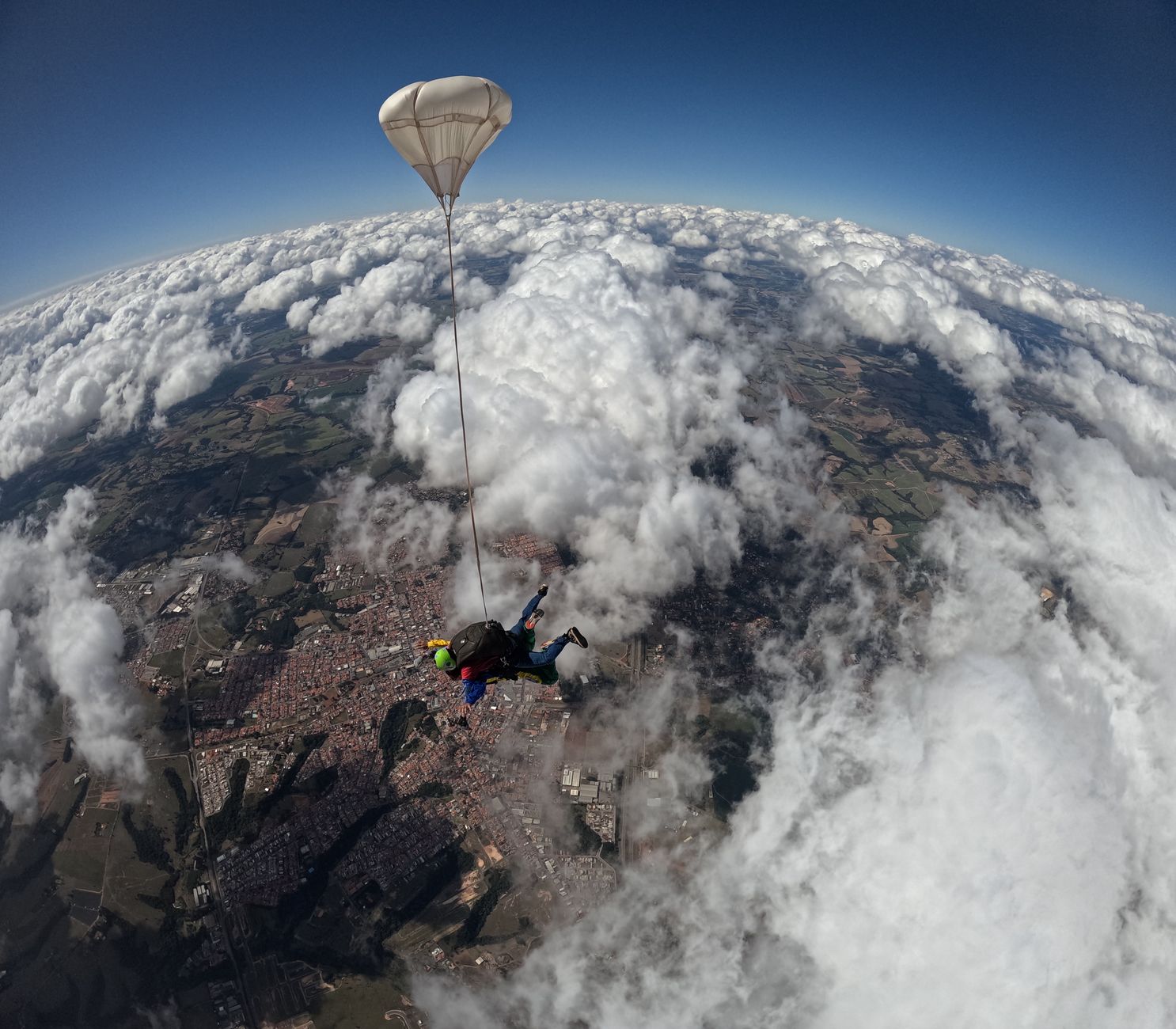 Skydiver z otwartym spadochronem unosi się nad chmurami i zabudowanymi terenami