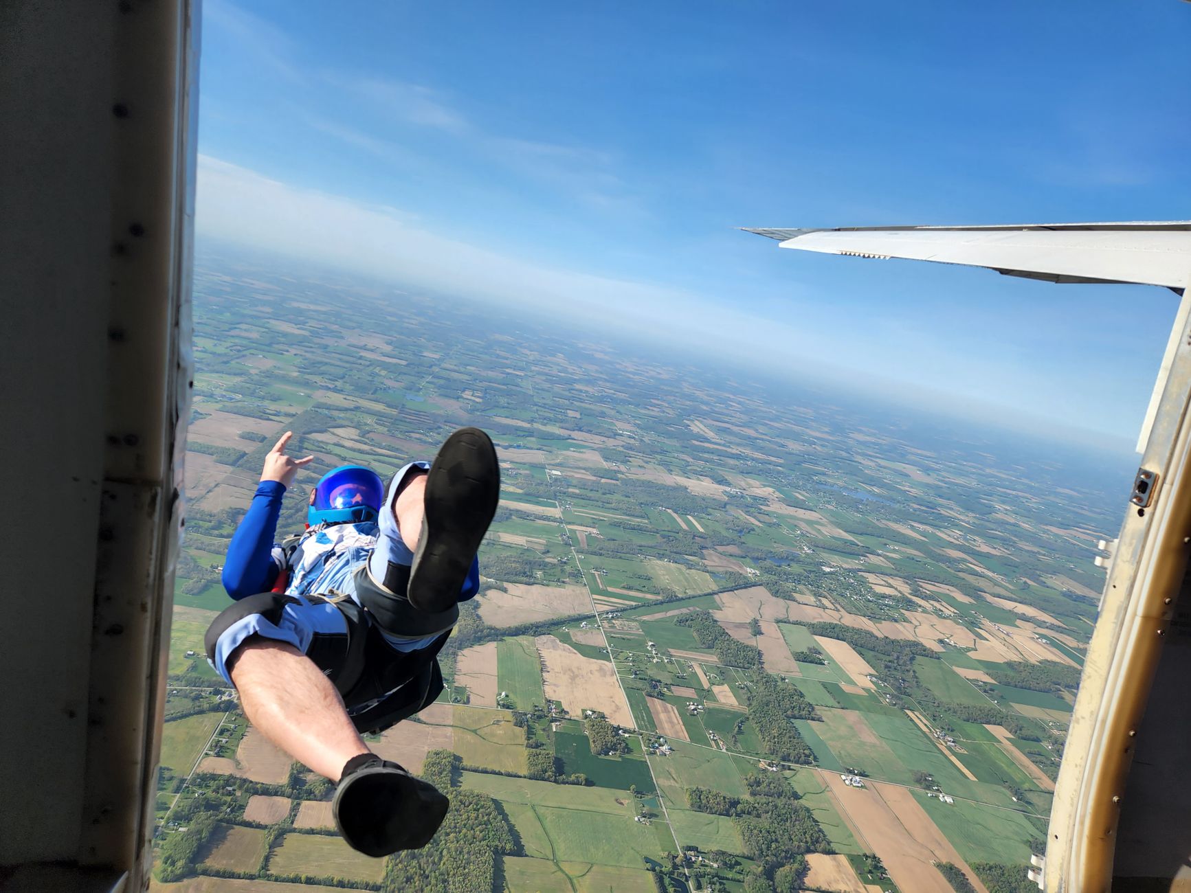 Skydiver w niebieskim kombinezonie skacze z samolotu nad zielonymi polami i łąkami