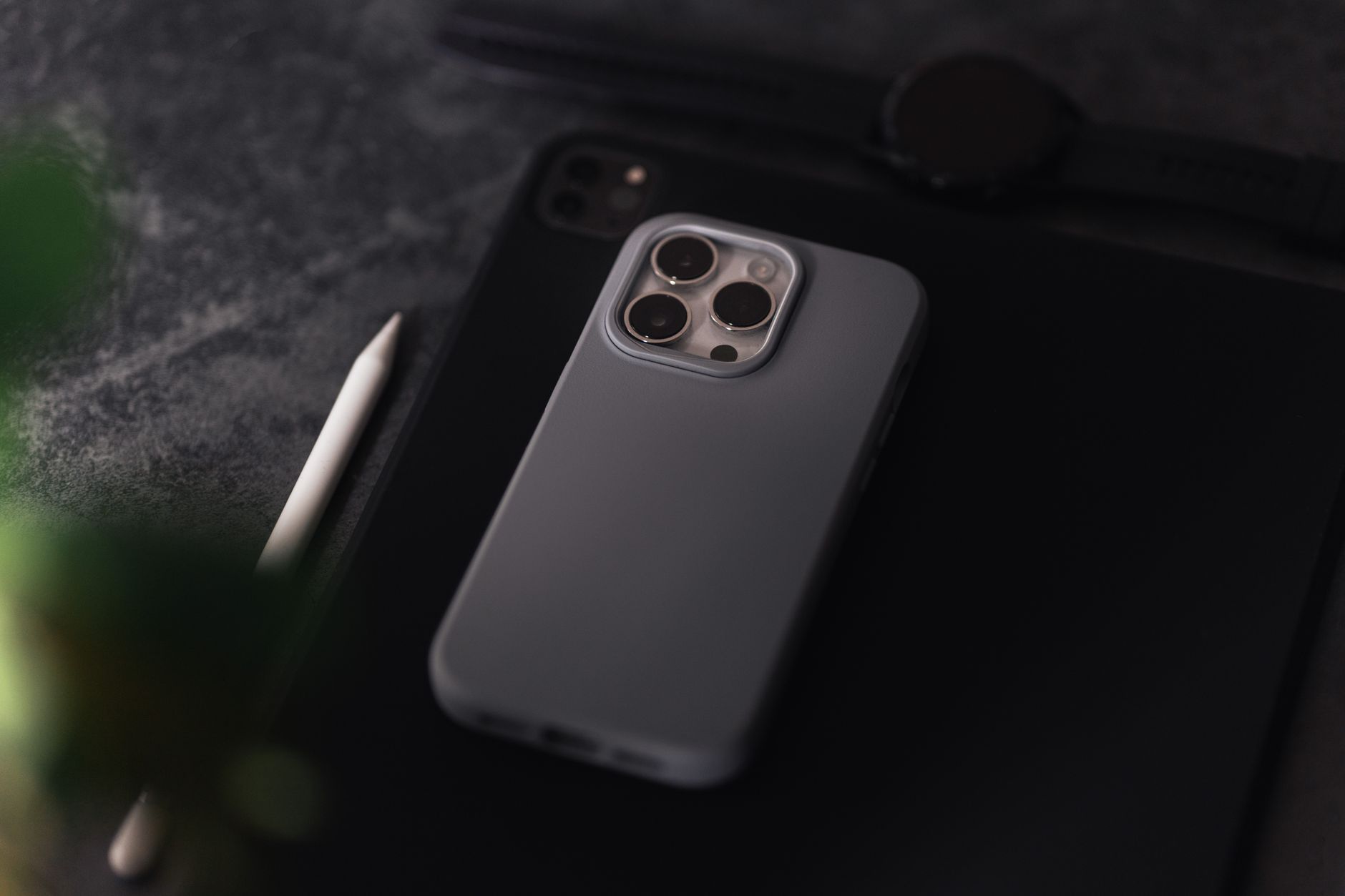 Czarny smartfon w etui ochronnym z aparatem czterokrotnym leżący na ciemnej powierzchni obok metalowego rysika